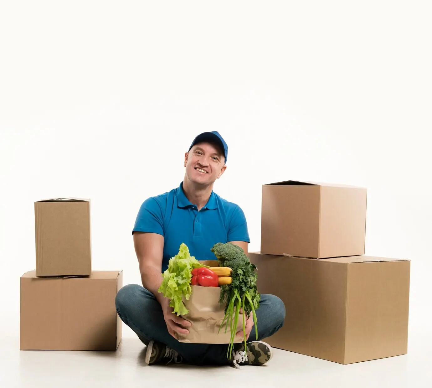 Курьер позирует с пакетом продуктов и картонными коробками.